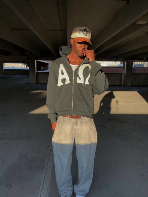 Man wearing the SĒK Apparel Alpha & Omega Zip Hoodie in dark gray — faith-inspired Christian zip-up hoodie with 'Alpha Omega' applique, in a parking garage