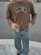 Man wearing the SĒK Apparel AMEN Appliqué Knit Crewneck in brown — premium faith-inspired streetwear sweatshirt with raised 'AMEN' appliqué text, styled outdoors
