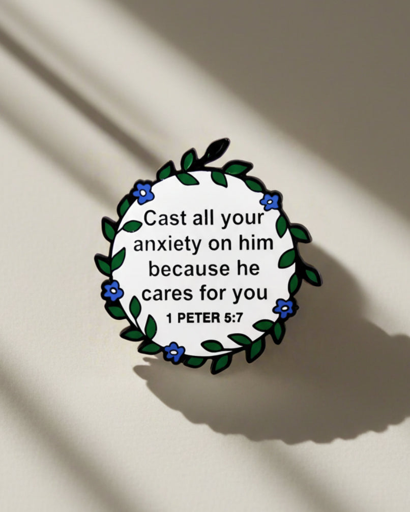 SĒK Apparel 1 Peter 5:7 enamel pin — floral Christian lapel pin with 'Cast all your anxiety on Him' scripture, front view on white background