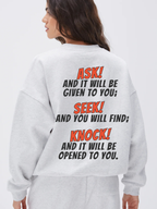 Woman wearing the SĒK Apparel Ask, Seek, Knock Crewneck in gray — back view showing Matthew 7:7 Bible verse graphic on white background