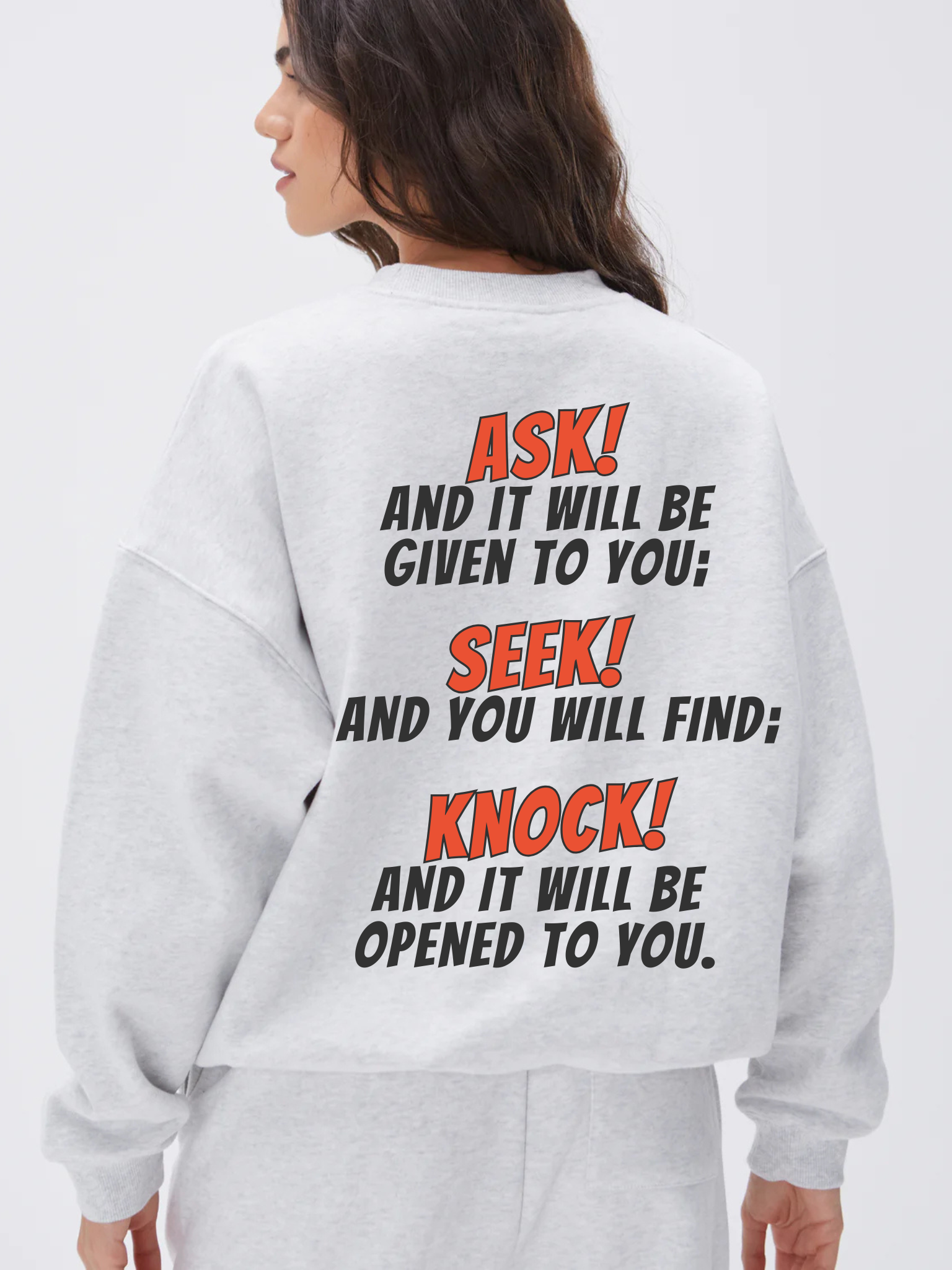 Woman wearing the SĒK Apparel Ask, Seek, Knock Crewneck in gray — back view showing Matthew 7:7 Bible verse graphic on white background