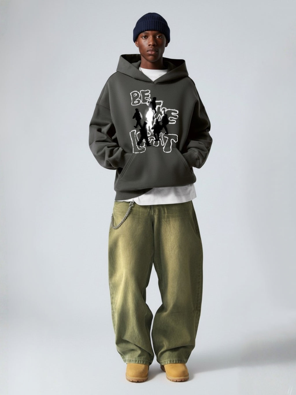Man wearing the SĒK Apparel Be the Light Hoodie in dark gray with green pants and beanie — scripture-inspired streetwear hoodie