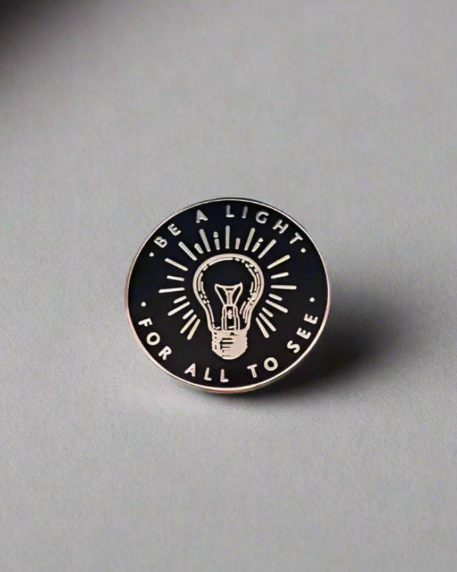 SĒK Apparel Be a Light enamel pin — gold and white Christian enamel pin with 'Be a Light' text, front view on white background