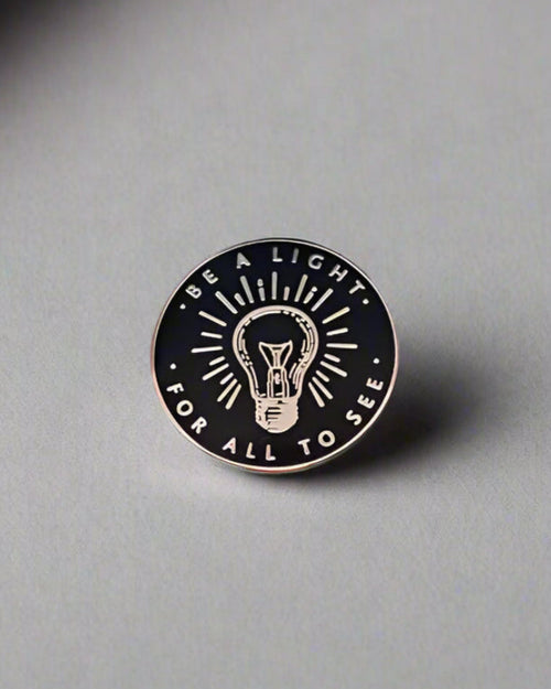 SĒK Apparel Be a Light enamel pin — gold and white Christian enamel pin with 'Be a Light' text, front view on white background