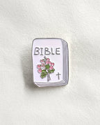 SĒK Apparel Bible enamel pin — brooch shaped like a Bible with floral design and cross detail, faith-inspired Christian lapel pin