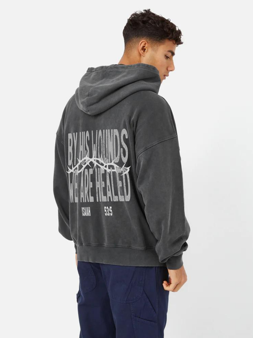 Man wearing the SĒK Apparel By His Wounds Hoodie — back view of washed black Christian hoodie with 'By His Wounds' scripture graphic