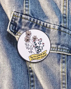SĒK Apparel By His Wounds enamel pin — floral Christian lapel pin with Isaiah 53:5 scripture verse, shown pinned to denim fabric