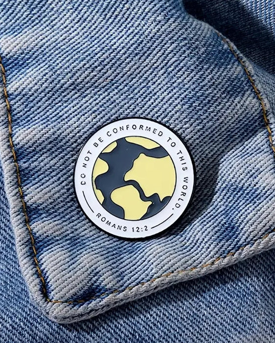 A pin with a yellow and black design featuring the text 'DO NOT CONFORM' and a citation 'ROMANS 12:2' on a denim fabric.