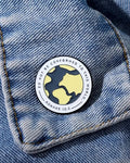 A pin with a yellow and black design featuring the text 'DO NOT CONFORM' and a citation 'ROMANS 12:2' on a denim fabric.