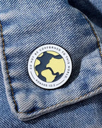 A pin with a yellow and black design featuring the text 'DO NOT CONFORM' and a citation 'ROMANS 12:2' on a denim fabric.