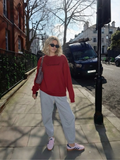 Woman wearing the SĒK Apparel Emmanuel Monochromatic Crewneck in red — faith-inspired Christian sweatshirt with embroidered 'Emmanuel' text, styled outdoors on a city sidewalk