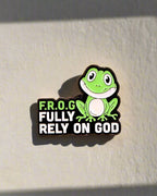 A pin with a cartoon image of a frog and the text 'F.R.O.G. FULLY RELY ON GOD' on it.