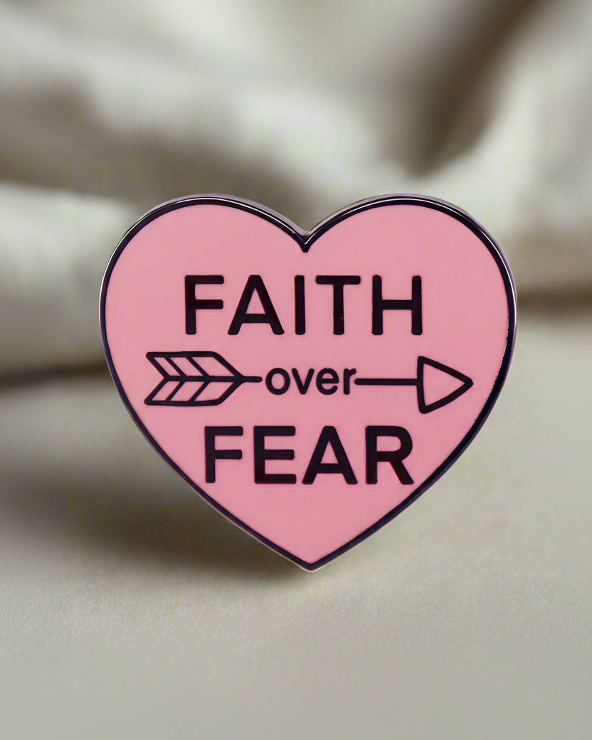 A pin with a pink heart background and the text 'FAITH OVER FEAR' in white, along with a small arrow symbol.