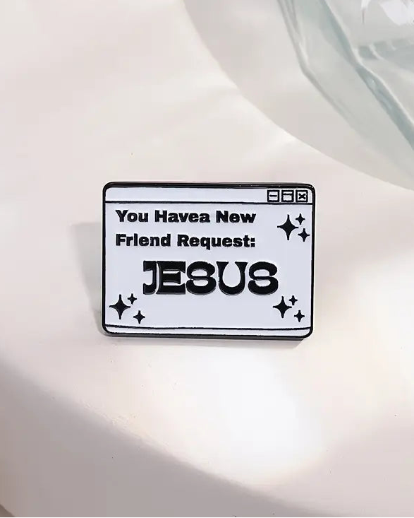 A pin with the text 'You Havea New Friend Request: JESUS' on a white surface.