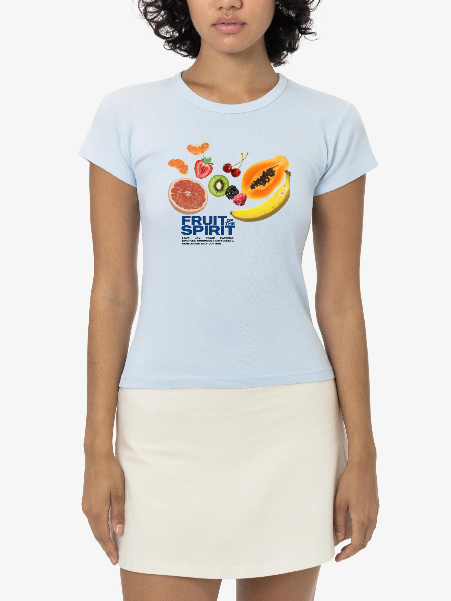 Woman wearing the SĒK Apparel Fruit of the Spirit Baby Tee in light blue — faith-inspired Christian graphic tee with fruit illustration referencing Galatians 5:22-23