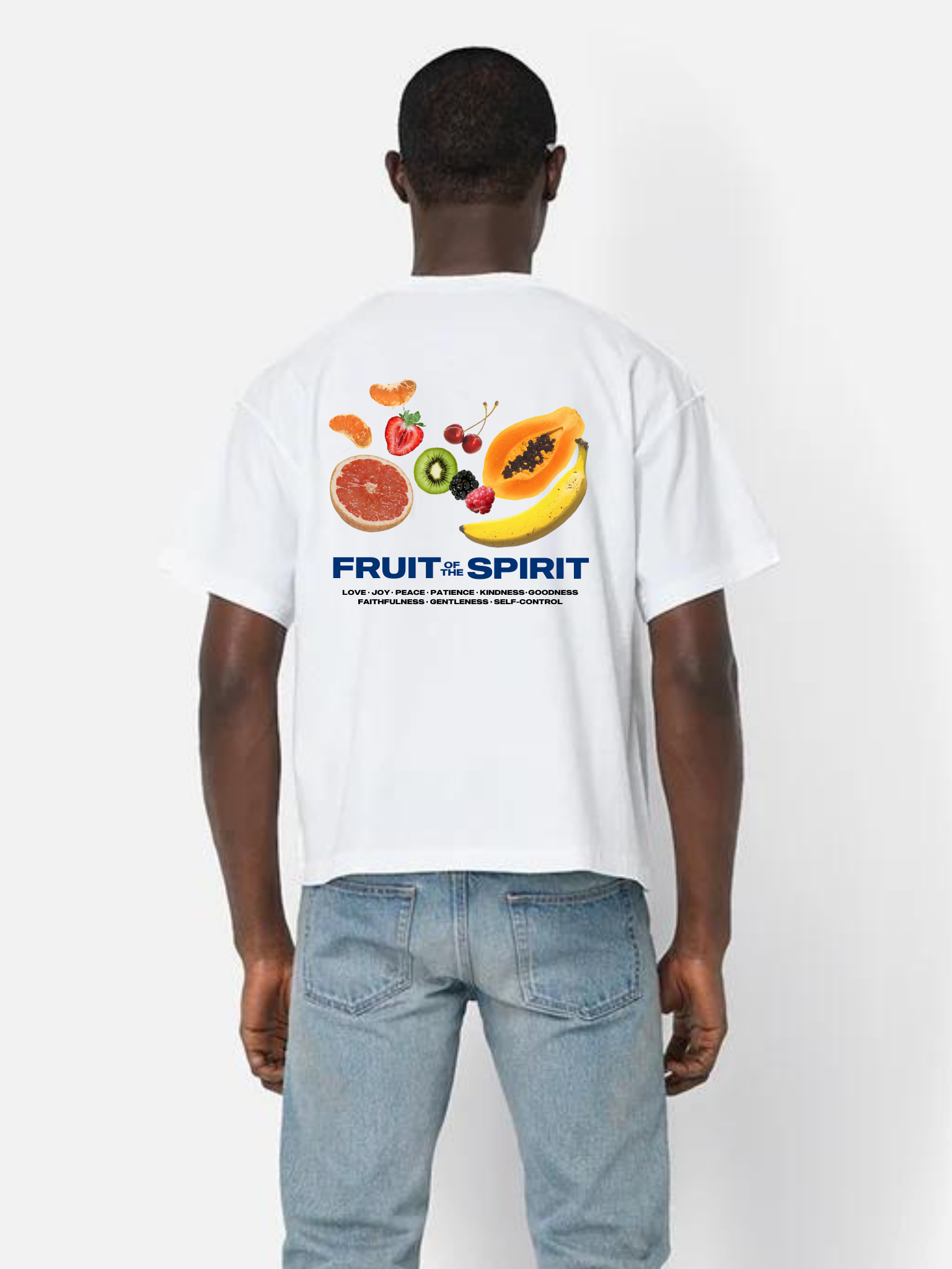 Man wearing the SĒK Apparel Fruit of the Spirit Box Tee in white — back view with fruit illustration and 'Fruit of the Spirit' Galatians 5:22 graphic