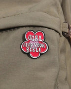 SĒK Apparel Girl, Read Your Bible enamel pin — faith-inspired Christian lapel pin encouraging scripture reading, front view on a backpack
