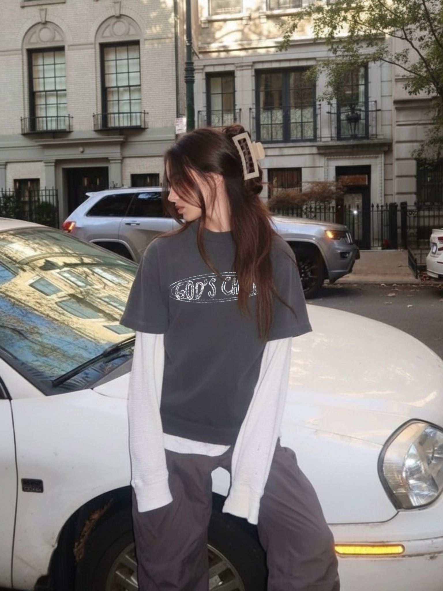Woman wearing the SĒK Apparel God's Child 2Fer Long Sleeve in dark gray — faith-inspired Christian streetwear with 'God's Child' text, styled outdoors on a city street