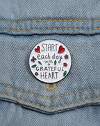 SĒK Apparel Grateful Heart enamel pin — round floral Christian lapel pin with 'Grateful Heart' text and heart details, faith-inspired accessory