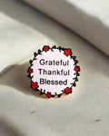 SĒK Apparel Grateful, Thankful, Blessed enamel pin — round floral Christian lapel pin with 'Grateful Thankful Blessed' text, faith-inspired accessory