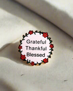 SĒK Apparel Grateful, Thankful, Blessed enamel pin — round floral Christian lapel pin with 'Grateful Thankful Blessed' text, faith-inspired accessory