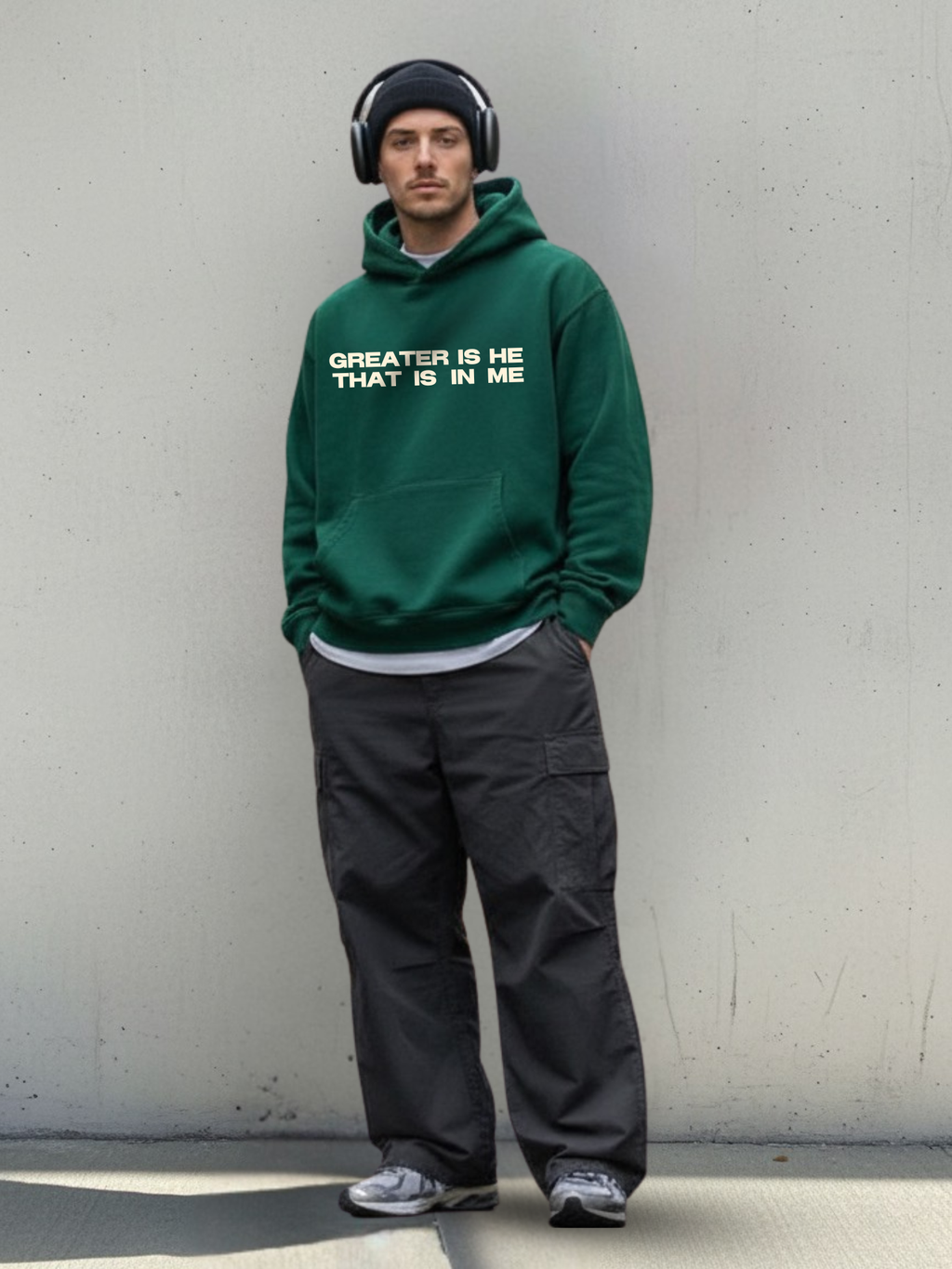 Man wearing a green hoodie with text and black pants against a plain wall