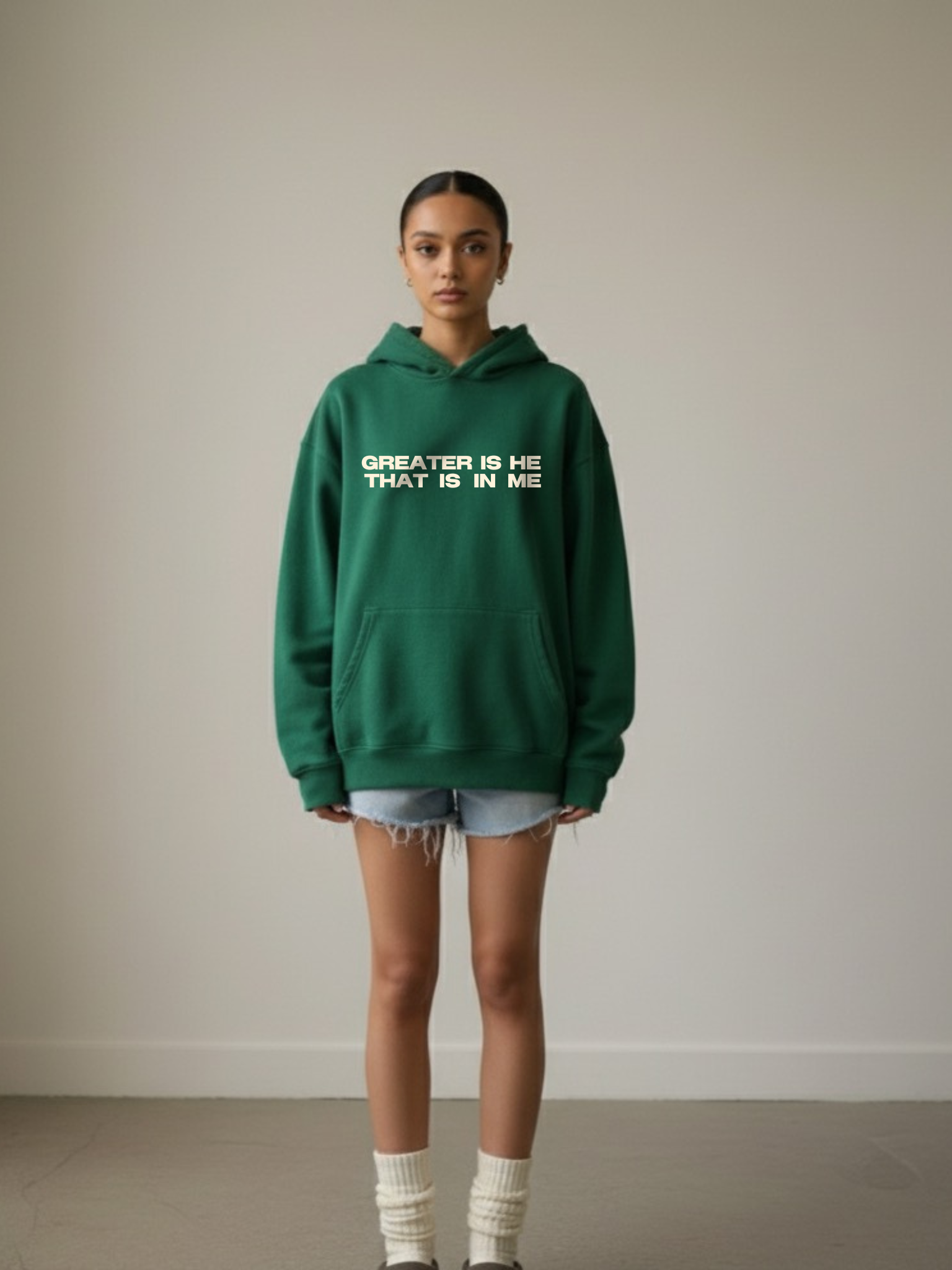 Woman wearing the SĒK Apparel Greater is He Hoodie in green — front view of faith-inspired Christian pullover hoodie with 'Greater is He That is in Me' text, referencing 1 John 4:4
