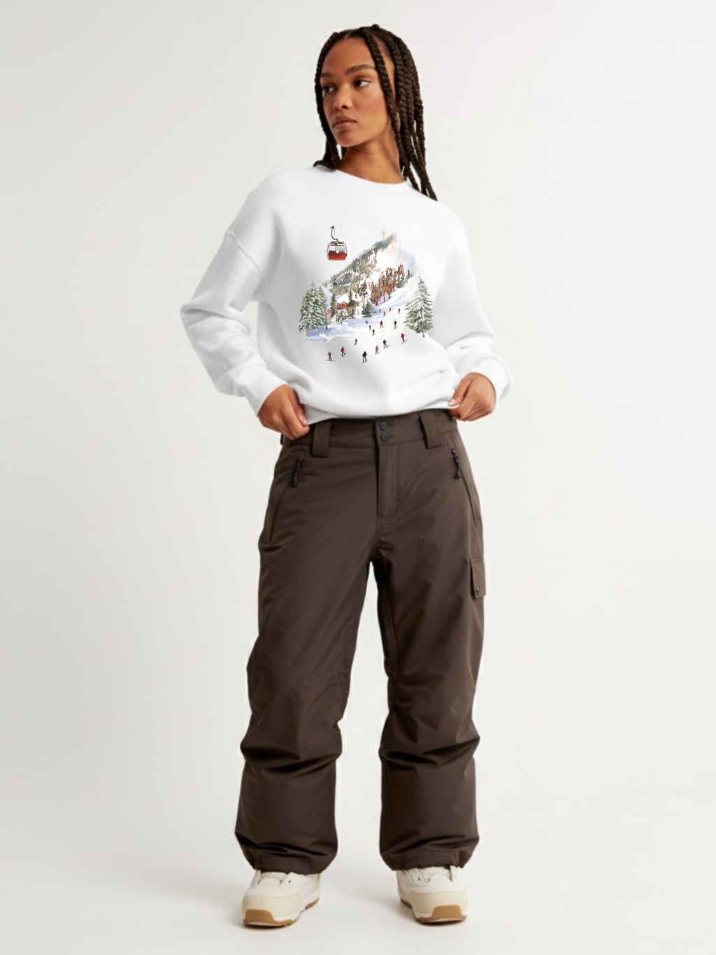 Woman wearing the SĒK Apparel Holy Hill Crewneck in white — faith-inspired Christian sweatshirt with Christmas village graphic design, styled with brown cargo pants