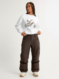 Woman wearing the SĒK Apparel Holy Hill Crewneck in white — faith-inspired Christian sweatshirt with Christmas village graphic design, styled with brown cargo pants