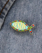SĒK Apparel ichthys enamel pin — fish-shaped Christian lapel pin with 'JESUS' text in center, shown pinned to denim fabric