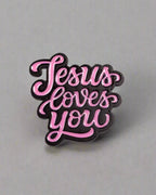 SĒK Apparel Jesus Loves You enamel pin — pink pin with 'JESUS LOVES YOU' in cursive letters, faith-inspired Christian lapel pin