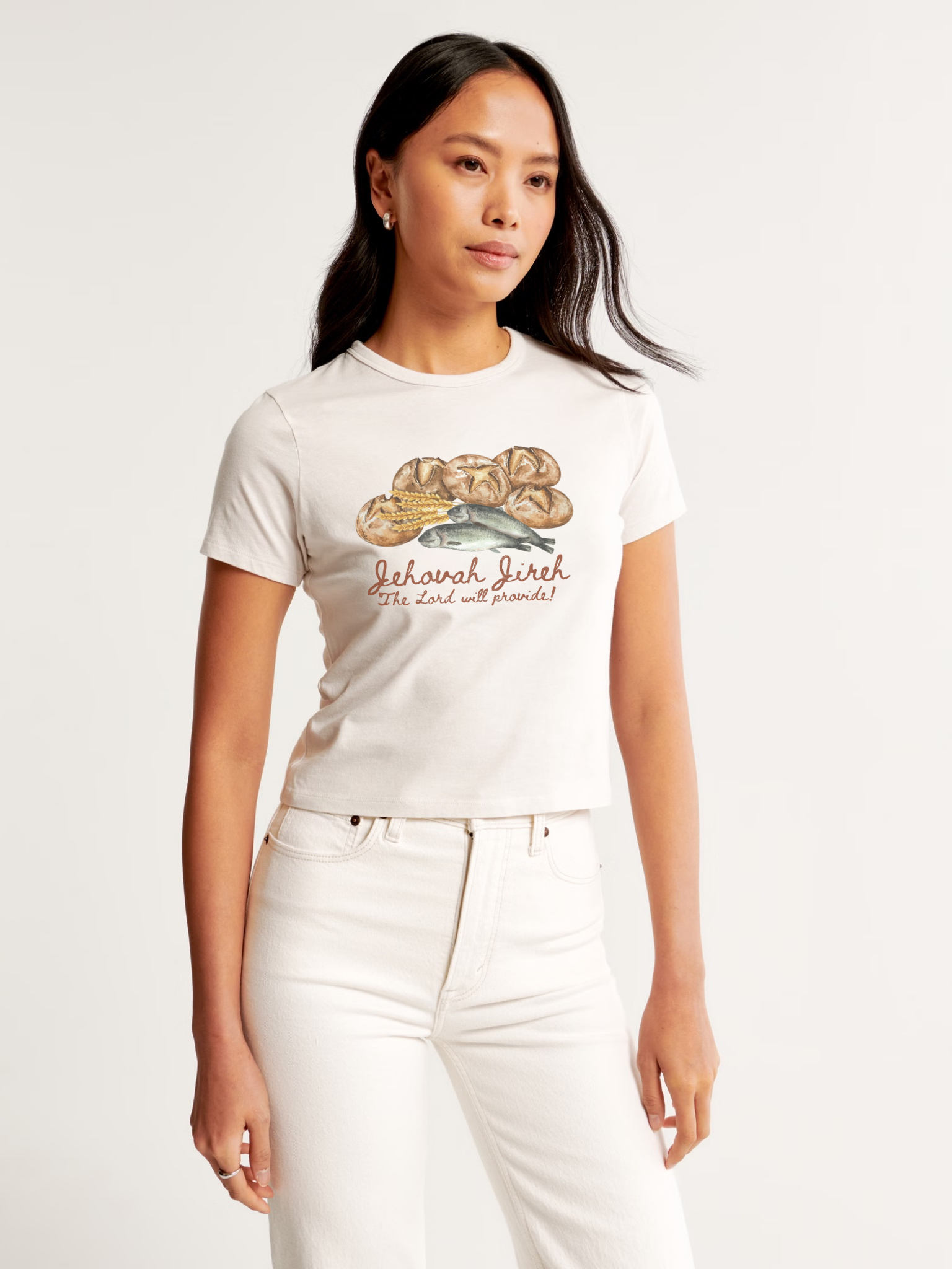 Woman wearing the SĒK Apparel Jehovah Jireh Baby Tee in off-white — front view of faith-inspired Christian graphic tee with 'The Lord Will Provide' design