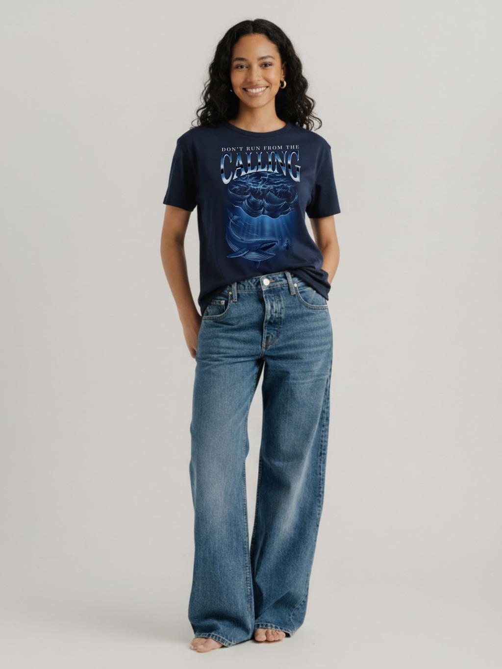 Woman wearing the SĒK Apparel Jonah Vintage Tee in navy — faith-inspired Christian graphic tee with Jonah and the whale illustration, styled with high-waisted jeans