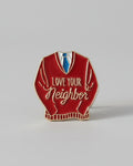 Red sweater-shaped pin with 'Love Your Neighbor' text on a gray background