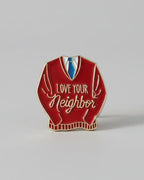Red sweater-shaped pin with 'Love Your Neighbor' text on a gray background