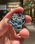 SĒK Apparel No Rain, No Flowers enamel pin — blue pin with watering can and floral illustration and 'No Rain No Flowers' text, faith-inspired Christian encouragement lapel pin