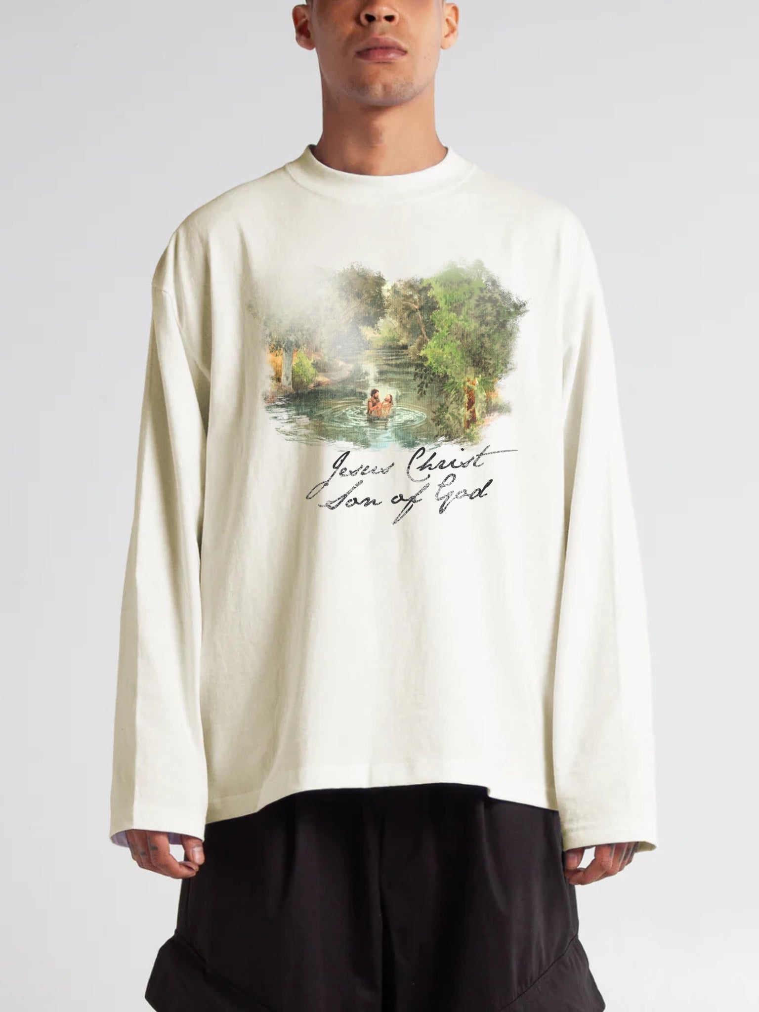 Man wearing the SĒK Apparel Son of God Long Sleeve in beige — front view of faith-inspired Christian graphic long sleeve tee with Jesus baptism artwork and 'Son of God' text, referencing Matthew 3:17