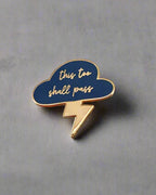 SĒK Apparel This Too Shall Pass enamel pin — blue cloud and lightning bolt design with 'This Too Shall Pass' text, faith-inspired Christian encouragement lapel pin