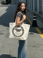 Woman carrying the SĒK Apparel Transformed Butterfly Tote on a street — faith-inspired Christian tote bag with butterfly graphic and 'Transformed' text, referencing Romans 12:2