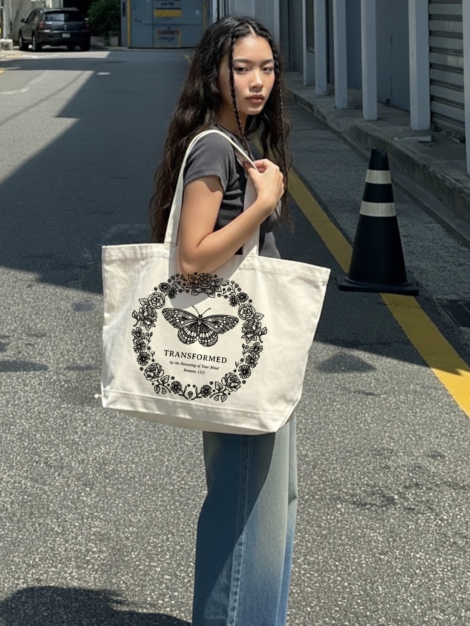 Woman carrying the SĒK Apparel Transformed Butterfly Tote on a street — faith-inspired Christian tote bag with butterfly graphic and 'Transformed' text, referencing Romans 12:2