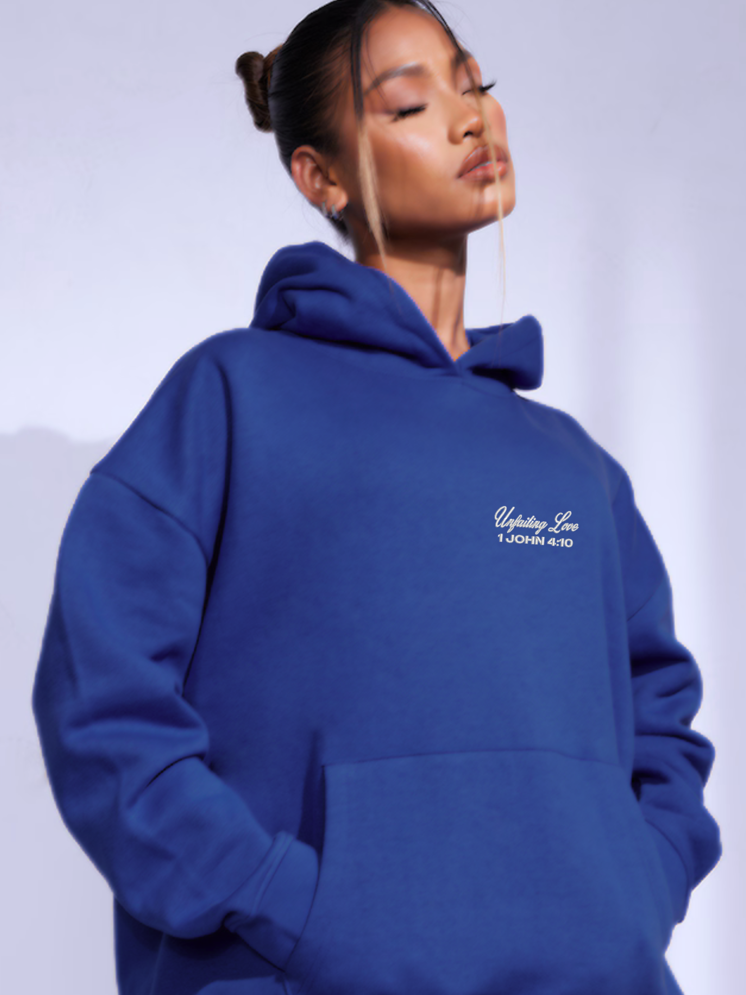 Woman wearing the SĒK Apparel Unfailing Love Hoodie in navy — front view of faith-inspired Christian pullover hoodie with embroidered 'Unfailing Love' text, referencing 1 John 4:10
