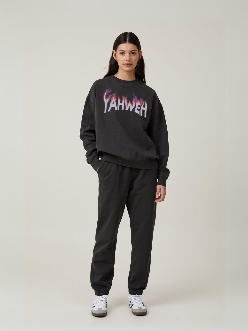 Woman wearing the SĒK Apparel YAHWEH Crewneck in gray — front view of faith-inspired Christian sweatshirt with bold 'YAHWEH' text, styled with black pants