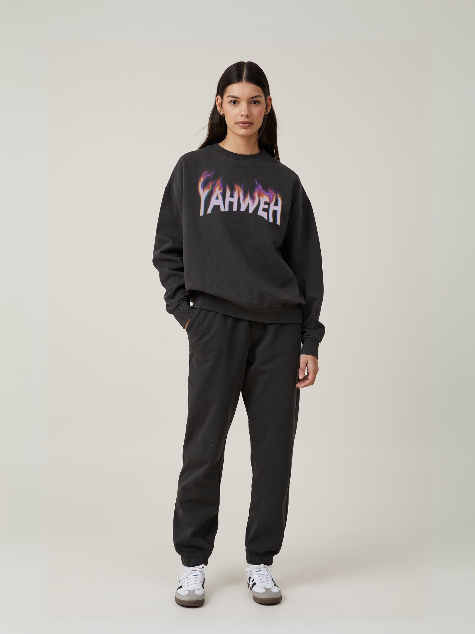 Woman wearing the SĒK Apparel YAHWEH Crewneck in gray — front view of faith-inspired Christian sweatshirt with bold 'YAHWEH' text, styled with black pants