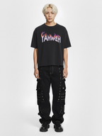 Man wearing the SĒK Apparel YAHWEH Tee in black — front view of faith-inspired Christian graphic tee with colorful 'Yahweh' flame-style text, styled with black pants